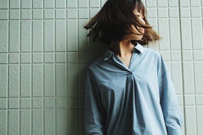 Young woman tossing hair while standing against wall