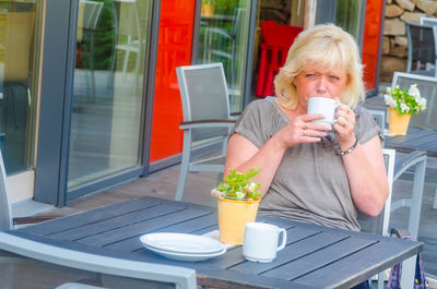 Portrait of woman drinking coffee while sitting at sidewalk cafe