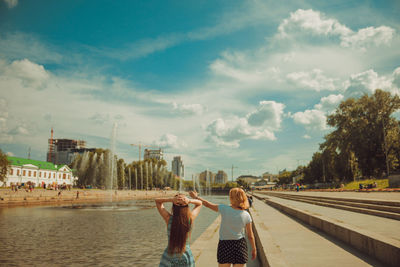 Rear view of women standing on bridge against cloudy sky