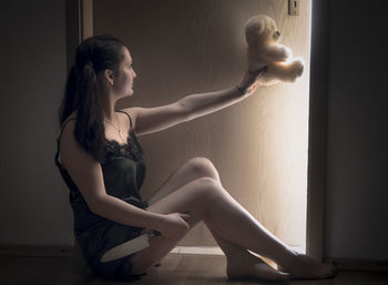 Young woman with teddy bear sitting at home