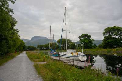 Sailboats moored on riverbank against sky