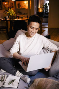 Smiling man using laptop while sitting on sofa in living room at home