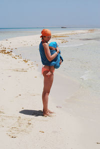 Rear view of mother holding her baby in wrap at beach