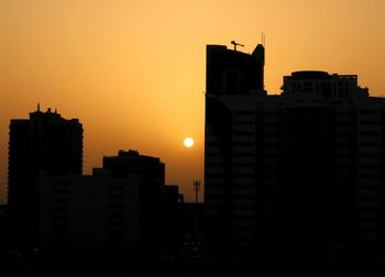 Silhouette buildings against orange sky during sunset