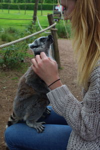 Young woman stroking lemur while sitting on field at park