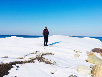 Man standing on snow covered shore against sky