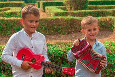 Brothers playing musical instruments while standing in park