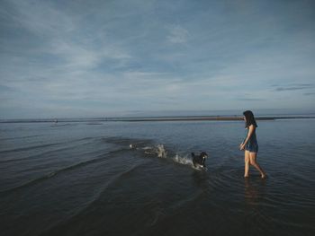 Woman with dog walking on shore at beach against sky