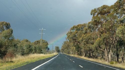 Country road amidst trees against sky