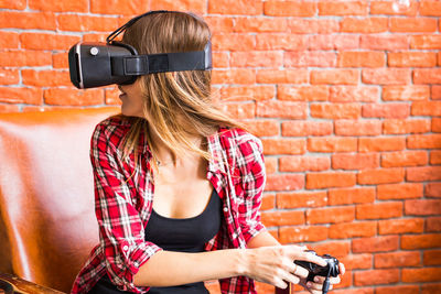 Young woman using mobile phone against brick wall