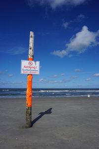 Information sign on wooden post at beach against sky