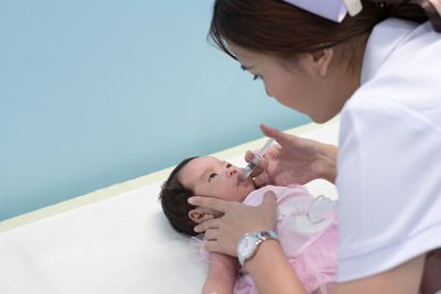 Side view of nurse giving vaccination through syringe to baby girl