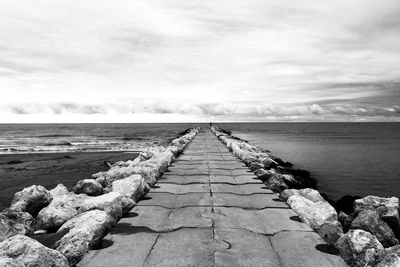 Pier on sea against cloudy sky