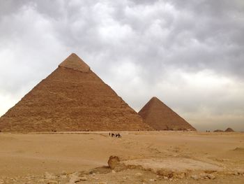 Pyramid in desert against cloudy sky