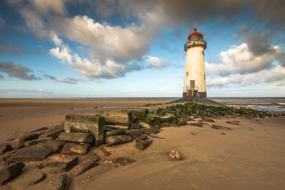 Lighthouse on beach by sea against sky