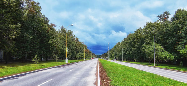 Empty road amidst trees against sky