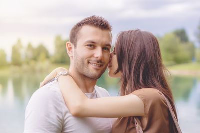 Portrait of smiling boyfriend with loving girlfriend against lake