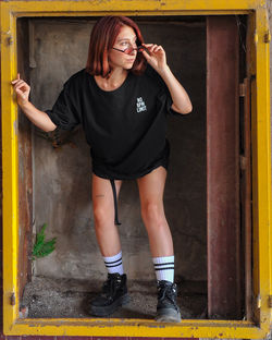 Full length portrait of young woman standing against wall