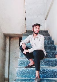 Portrait of young man sitting on staircase against wall
