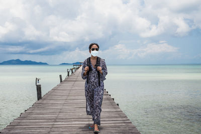 Woman in protective  mask standing on pier over sea against sky