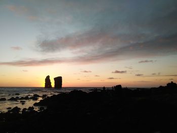 Silhouette rocks on shore against sky during sunset