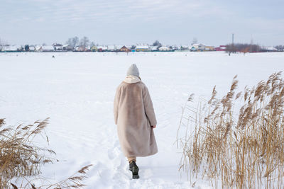 Young girl in beige clothes, fur coat made of artificial fur walks in winter