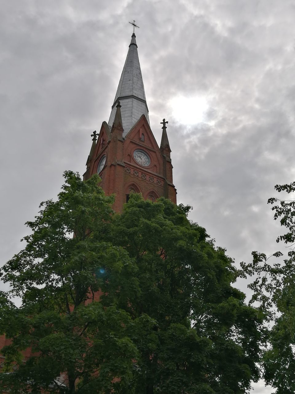 religion, tree, place of worship, spirituality, low angle view, sky, cloud - sky, tower, architecture, green color, day, clock tower, outdoors, built structure, no people, history, building exterior, cross, nature, bell tower