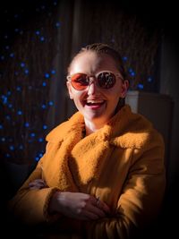 Portrait of cheerful young woman wearing sunglasses and coat at home