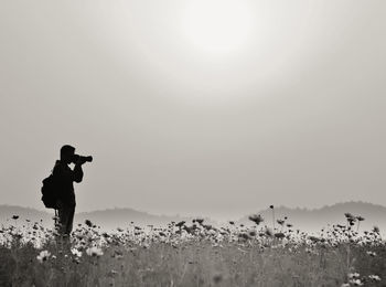 Silhouette man photographing on field against clear sky during sunny day