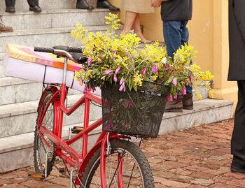Bicycle with flowers in basket while low section on people standing on steps in background