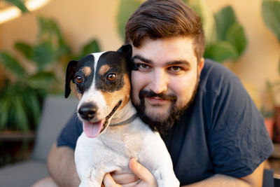 Friendly young man hugging his cute grocer dog and looking at camera. the dog has the tongue out 