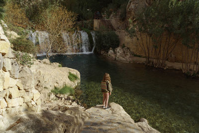 Rear view of girl standing on rock and looking away in water walls 