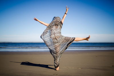 Young woman jumping on beach against clear sky