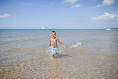 Cheerful boy running in sea against sky on sunny day