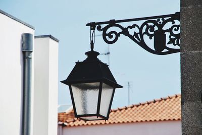 Low angle view of illuminated lamp hanging by building against sky