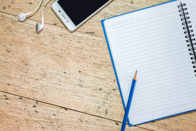 Directly above shot of blank open book with pencil and mobile phone on wooden table