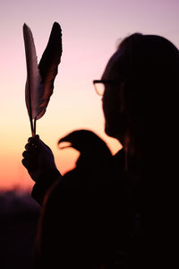 Silhouette of man and wild bird over sunset sky with feathers buzzard or eagle symbol of power