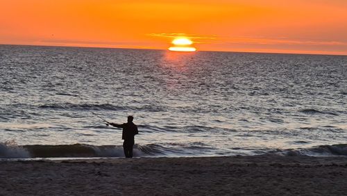 Silhouette man standing at beach against sky during sunset