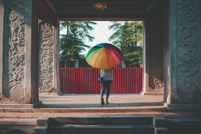 Rear view of man standing against multi colored umbrella