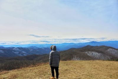 Rear view of man standing on mountain against sky