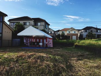 Houses on field by buildings against sky