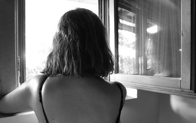 Rear view of woman looking through window at home