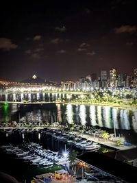 Illuminated buildings by river against sky at night