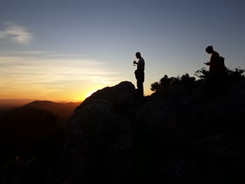 Silhouette man standing on rock against sky during sunset