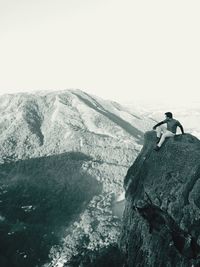 Man looking away sitting on mountain against sky