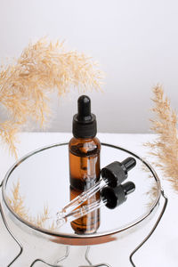 Glass bottle with pipette, scincare serum or essential oil and mirror surface with reflection