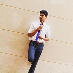 Young man wearing formals leaning on beige wall