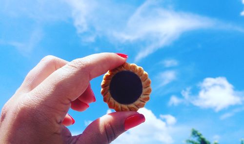 Cropped hand of woman holding biscuit against blue sky