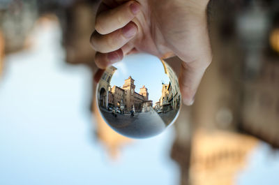 Cropped hand holding crystal ball with street and buildings reflection in city