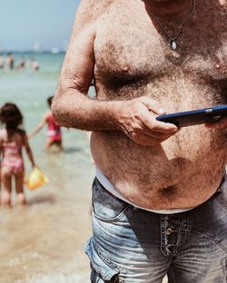 Midsection of man holding umbrella at beach